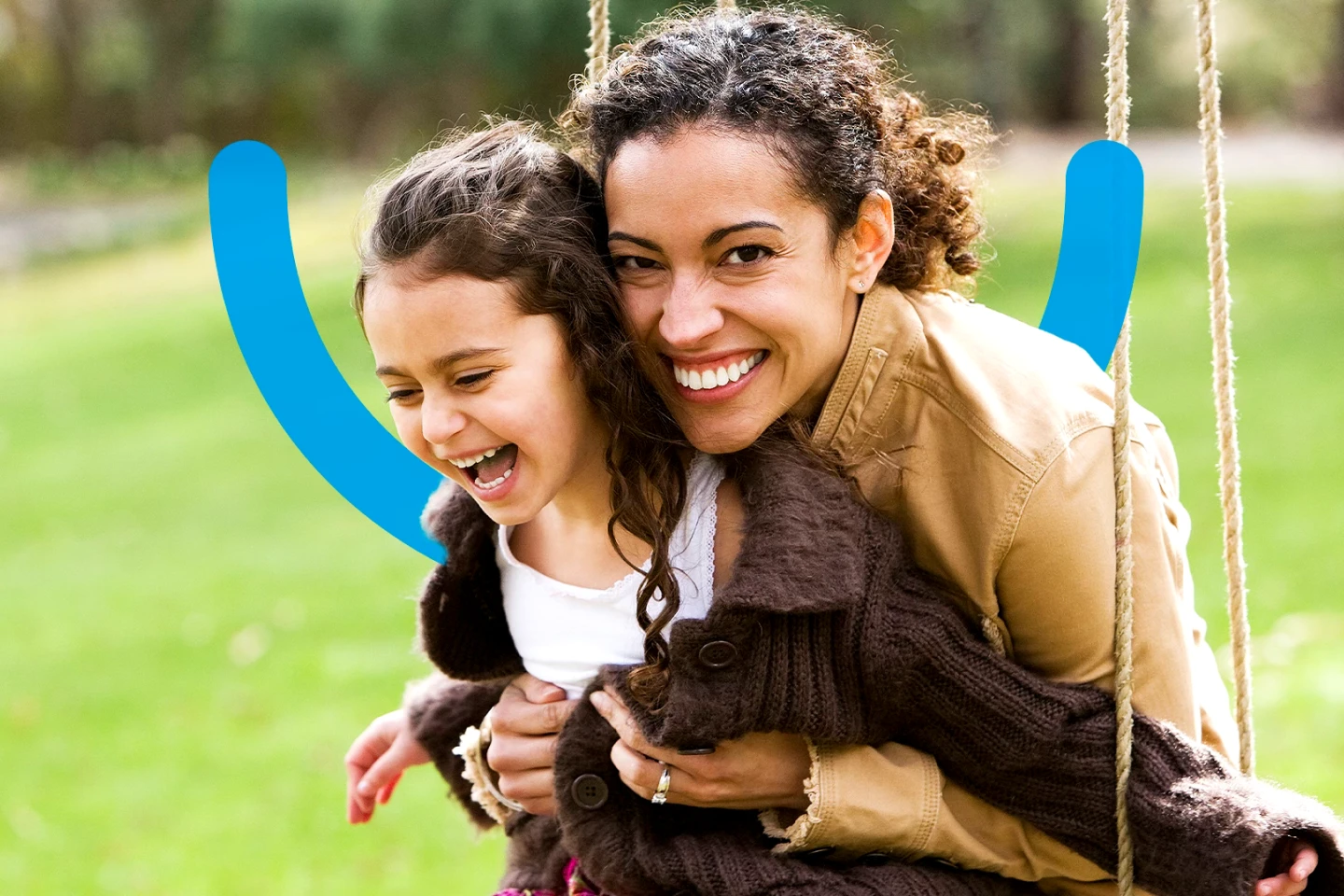 A mother and her little girl sharing a joyful moment on a swing in a park, showcasing a confident smile with an Aspen Dental smile icon behind them.