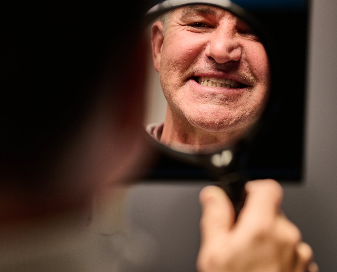 Older man smiling while looking at his teeth in a handheld mirror during a dental visit.