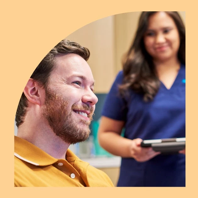 A man is smiling in front of a nurse who is holding a tablet