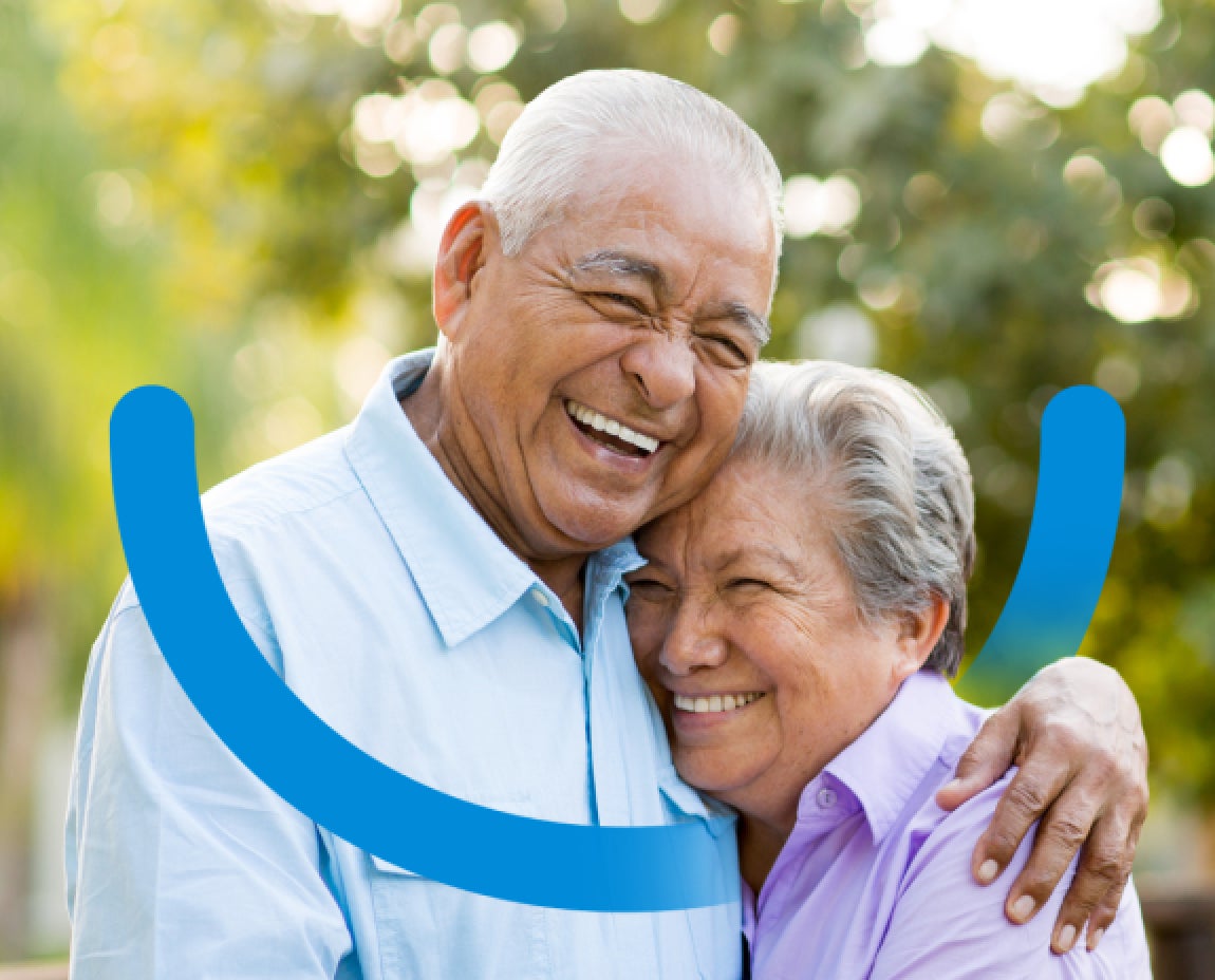 An older couple, both with gray hair, are smiling and embracing each other outdoors. A blue curved line overlays the image, forming a partial arc around them. Trees and greenery are visible in the background.