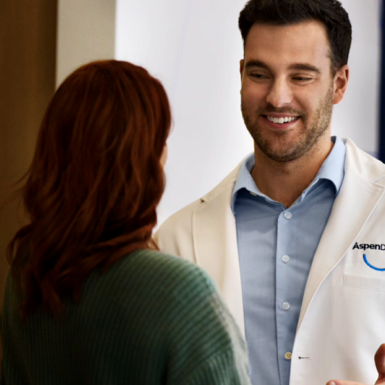 An Aspen Dental dentist in a white coat is conversing with a patient about her oral health.