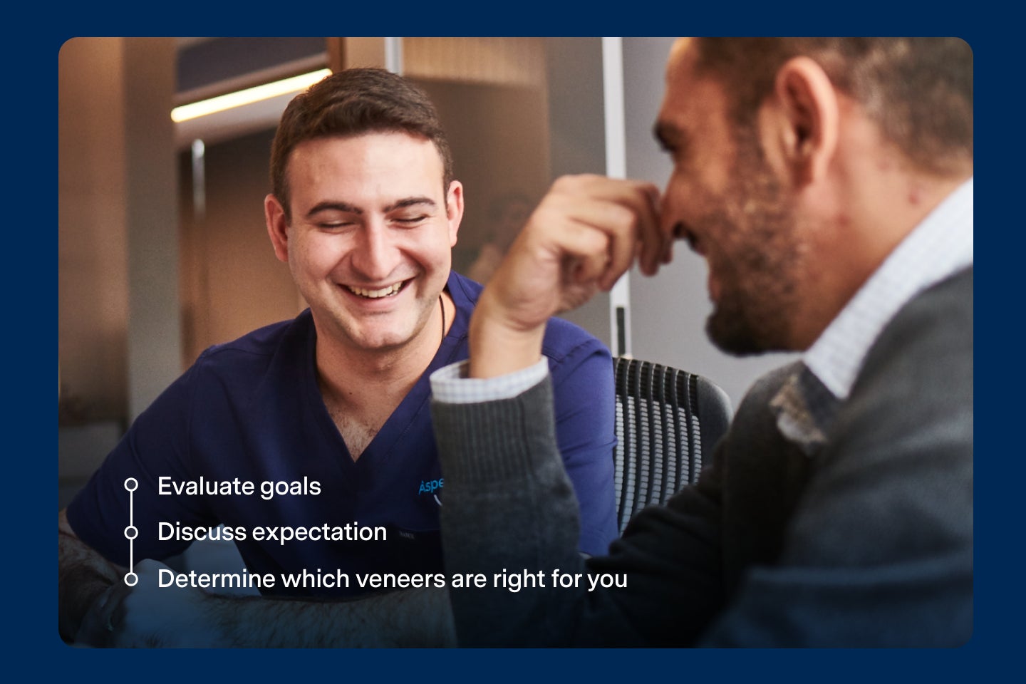 Two men sitting at a table, one in navy blue scrubs and the other in casual clothing, smiling and engaged in conversation. Three bullet points highlight during veneers consultation: evaluating goals, discussing expectations, and determining which is the right veneer type.