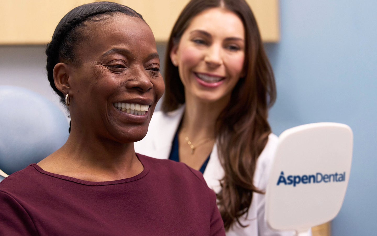 A happy patient smiles while holding a mirror after discussing how much a root canal costs with an Aspen Dental professional. The setting highlights affordable dental care and satisfaction with the treatment plan.