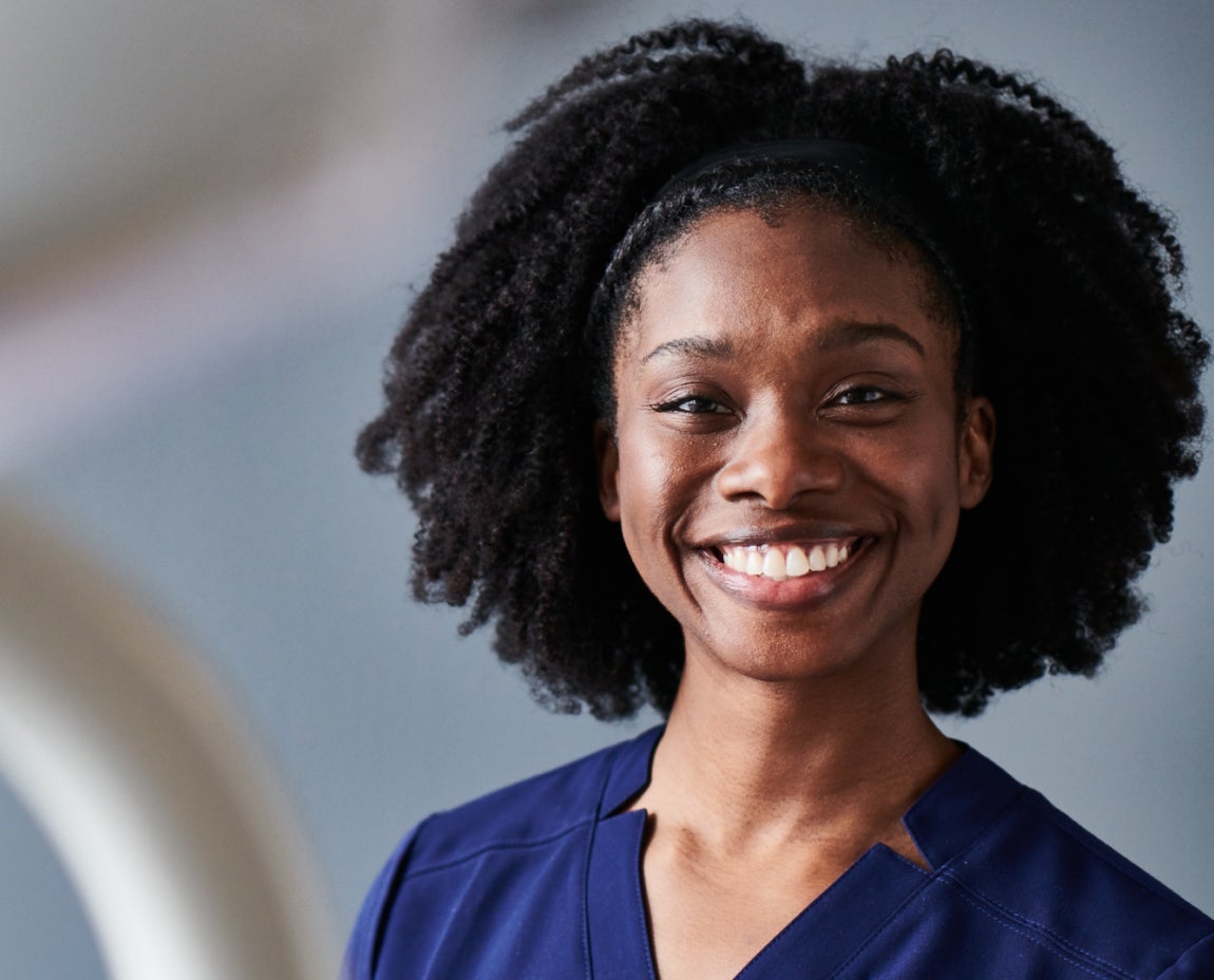 A smiling dental professional wearing navy scrubs, showcasing a friendly and welcoming demeanor in a dental care environment.
