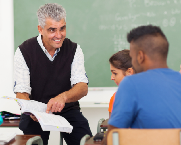 Confident and smiling senior male teacher engaging with young students in a classroom setting.