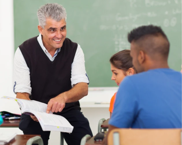 Confident and smiling senior male teacher engaging with young students in a classroom setting.