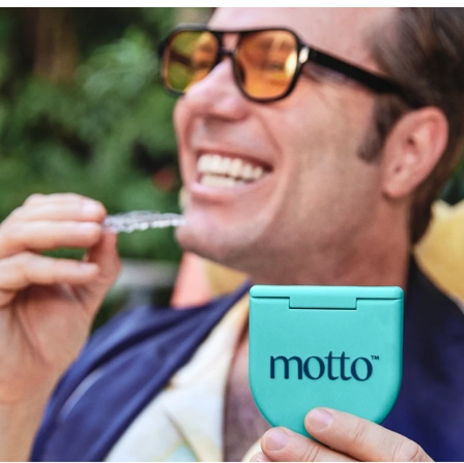 A man smiles while holding up a Motto Clear Aligners case. 