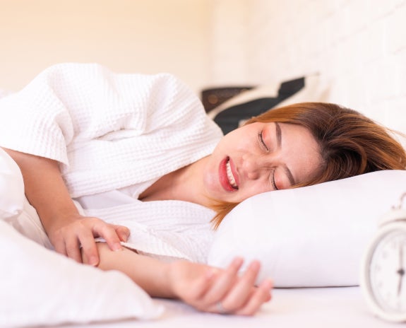 Woman sleeping in bed while clenching her teeth, indicating the condition of bruxism or teeth grinding, which can lead to dental issues like chipped teeth or jaw pain.