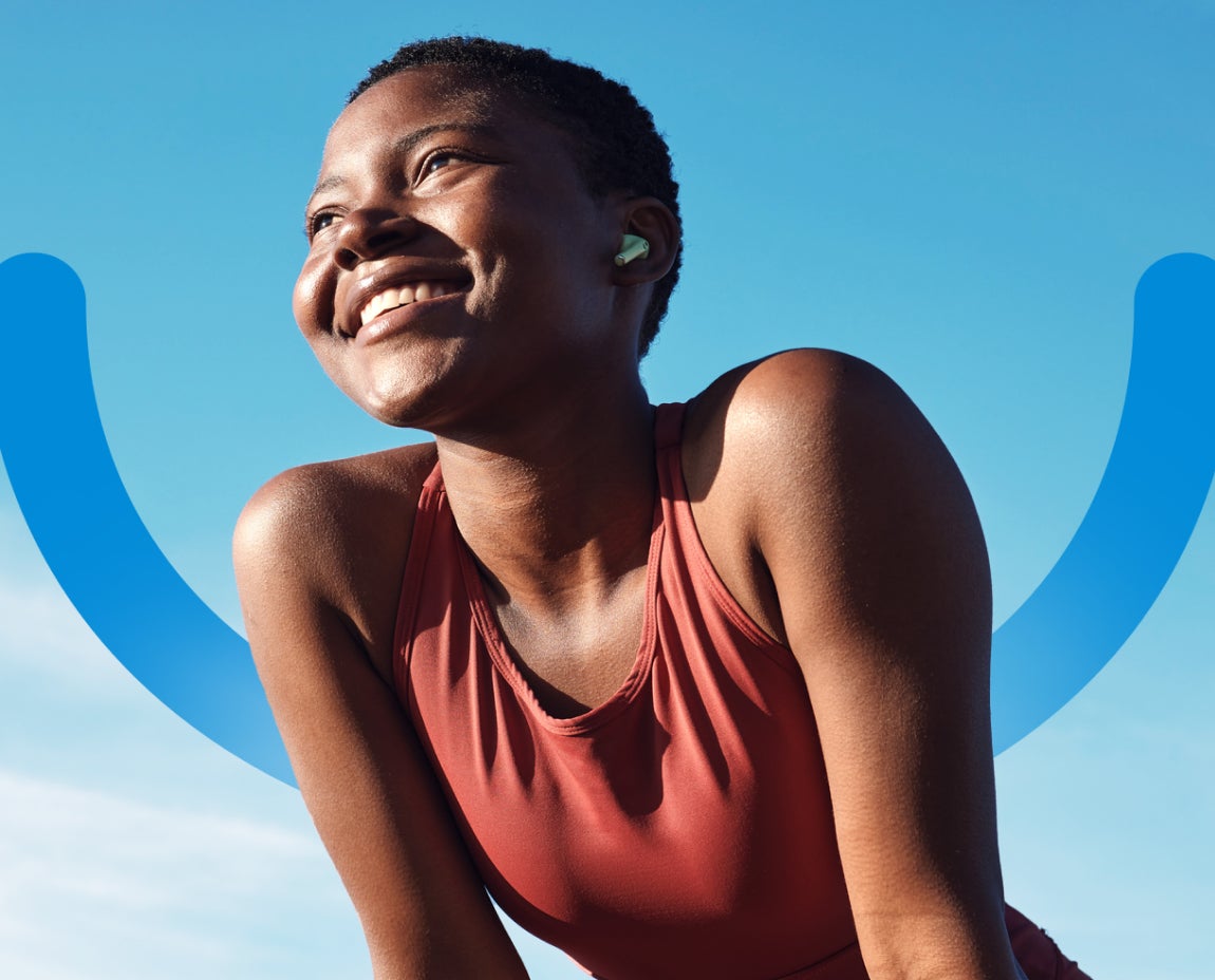 A person wearing a red tank top and earbuds smiles while leaning forward against a blue sky backdrop, with a blue curved line in the background.