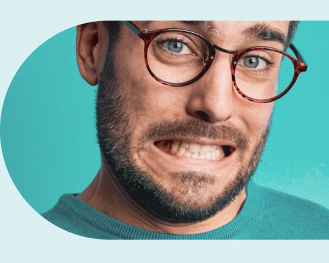 Man with glasses and beard grinding teeth with eyes wide open, against a turquoise background.