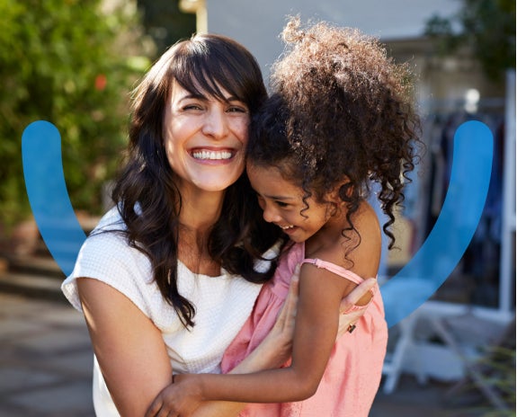 Two women joyfully laughing in front of a blue background with Aspen Dental smile icon, sharing a moment of happiness.