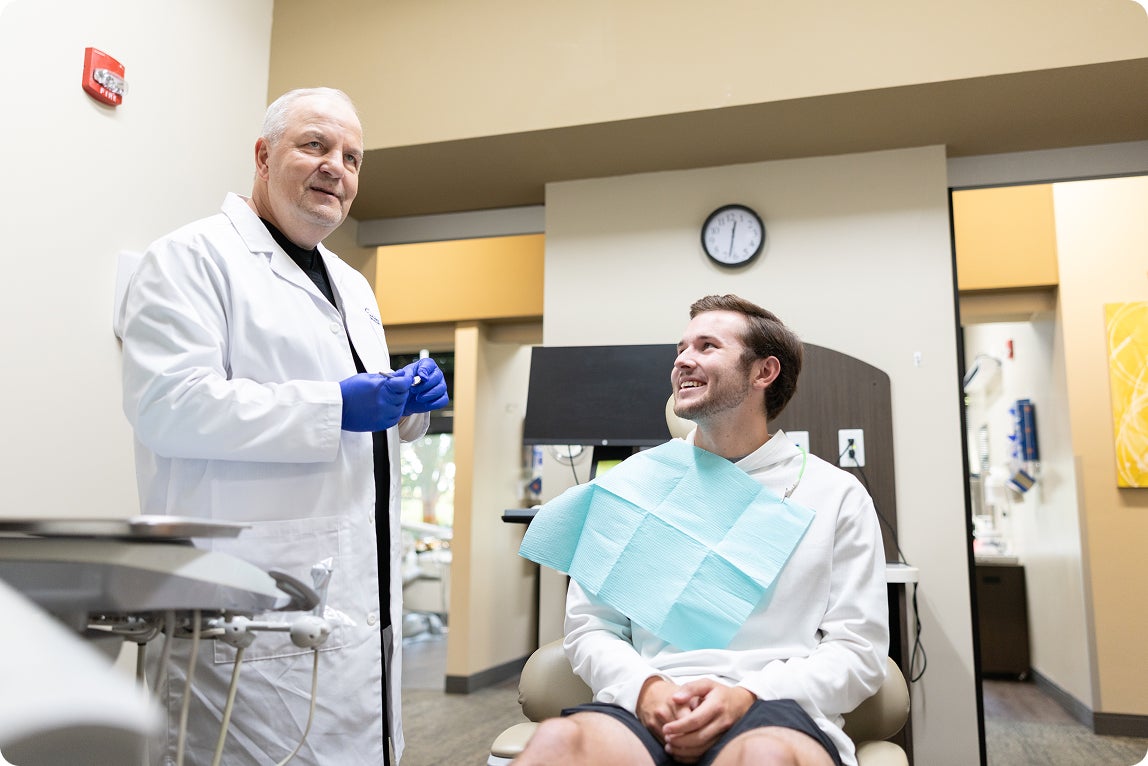 Jayden Fielding, Division I college football kicker, sitting in a dental chair as his ClearChoice prosthodontist provides personalized cleaning and maintenance tips for his dental implants, demonstrating the care and support ClearChoice patients receive throughout their implant journey.