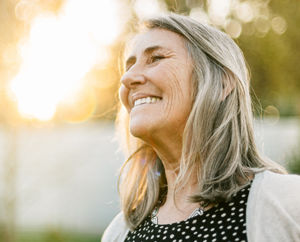 An older woman with gray hair smiling in the sun, radiating her confident smile.