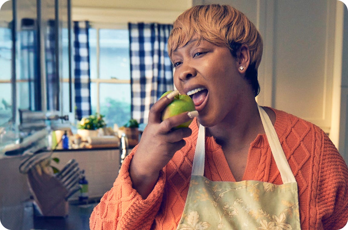 ClearChoice patient in an orange sweater and an apron, enjoying an apple after fully healing from her dental implant treatment.
