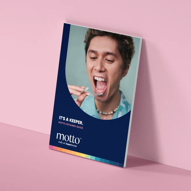 A man with a wide-open mouth is shown putting clear aligners on his teeth in a booklet titled 'Its a keeper. Motto retainer guide' placed against a wall.
