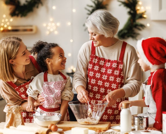 A group of people wearing aprons and santa hats are preparing cookies.