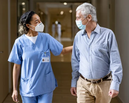 Un médico y un paciente caminan por un pasillo con máscaras puestas. 