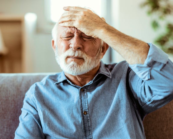 Elderly man sitting on a couch, holding his forehead in pain, illustrating the potential link between toothaches and headaches.