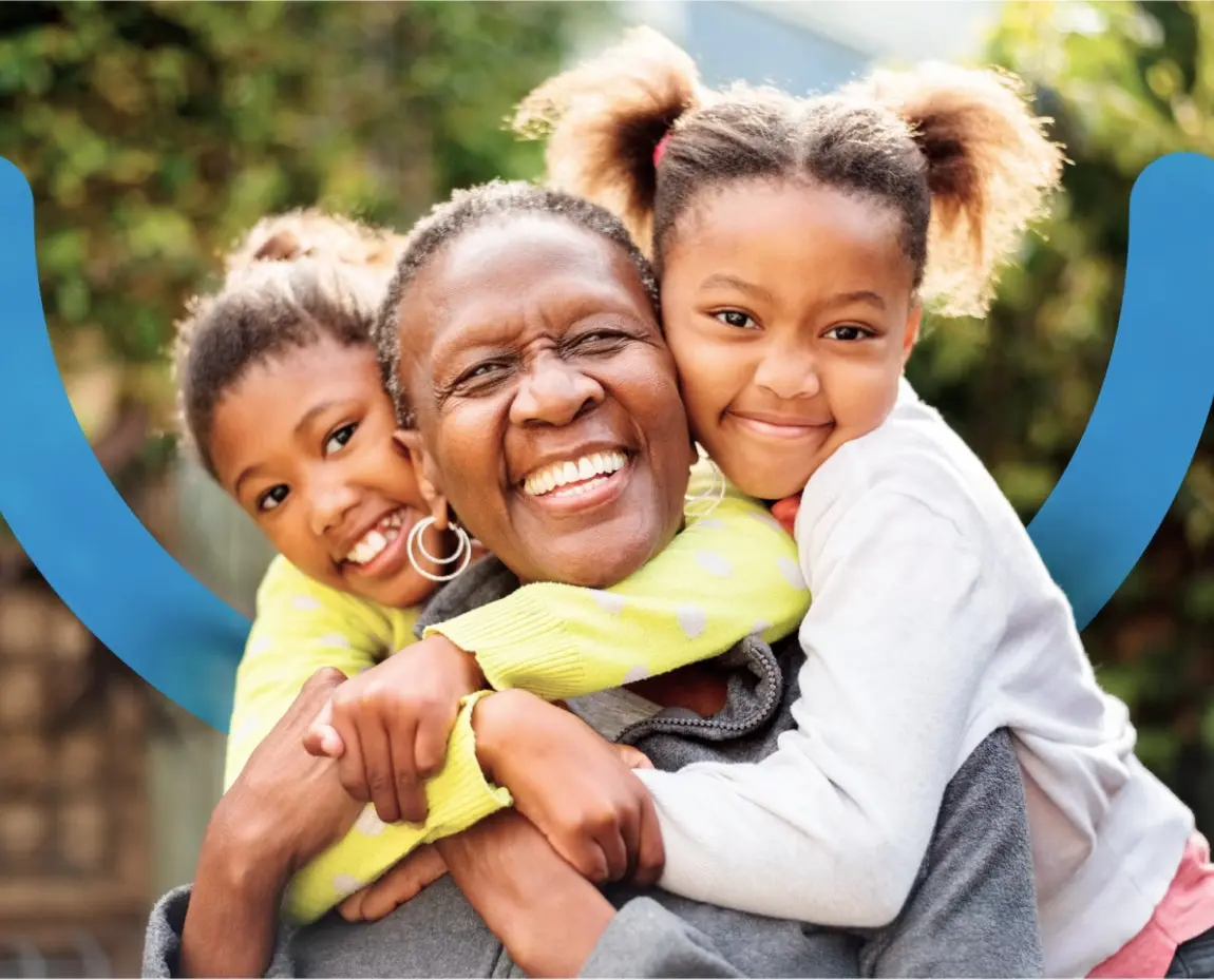 A joyful grandmother embracing her two smiling grandchildren outdoors, showcasing the confidence and happiness provided by Aspen Dental's care.