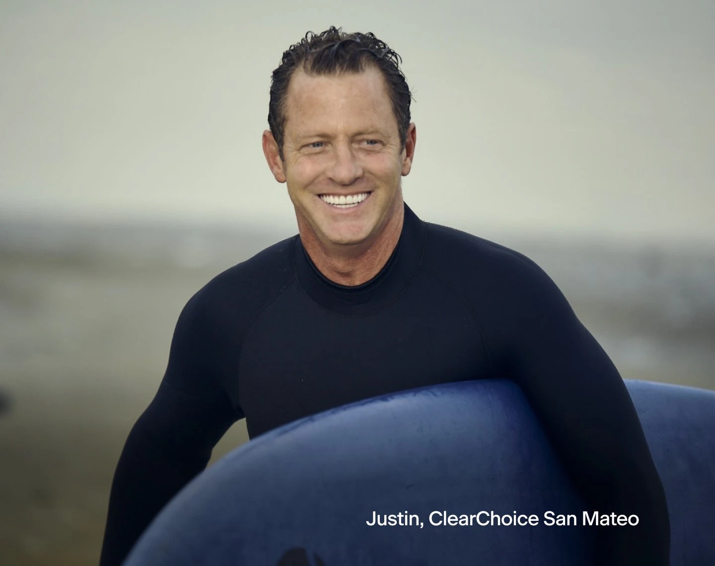A man in a wetsuit is holding a surfboard and smiling, in the bottom right corner is text that reads "Justin, ClearChoice San Mateo".