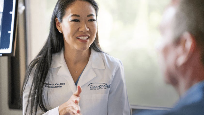 A woman in a white doctors coat with clear choice written on the front is talking to a male patient.