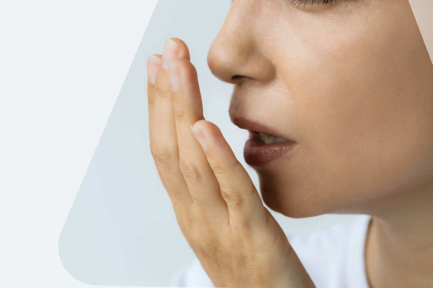 Image of a young woman discreetly checking her breath with hand over mouth. Addressing self-awareness and concern about potential bad breath.