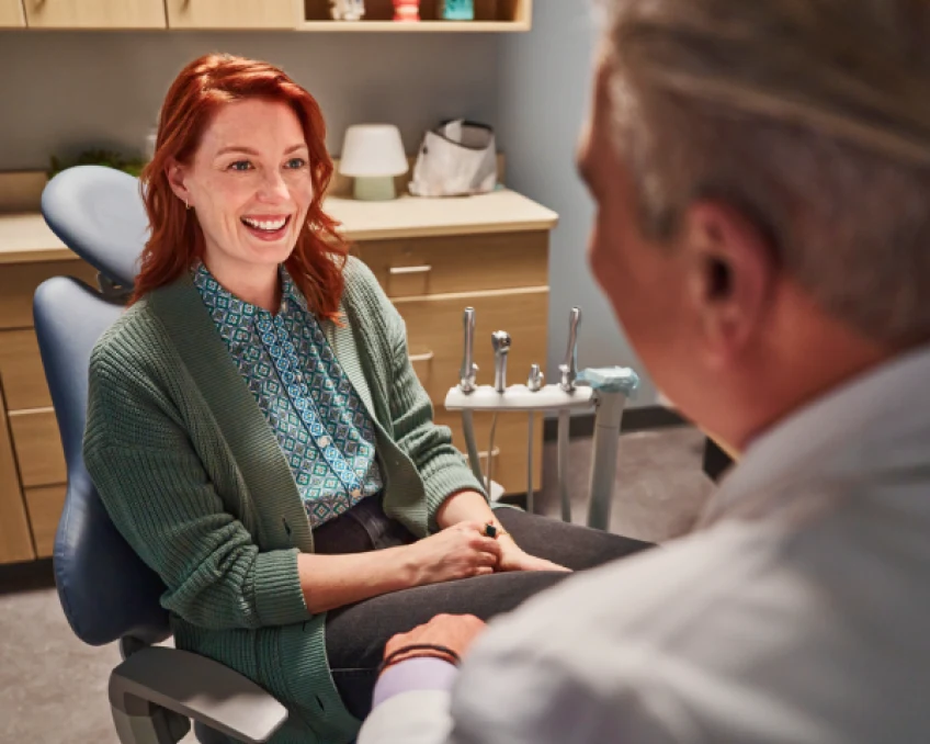  A woman having conversation with the dentist while seated in dentist chair.