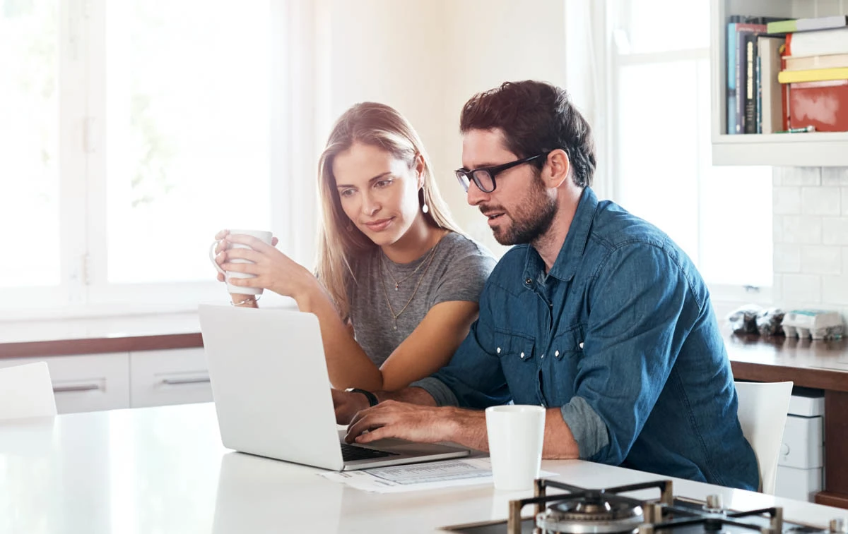 A couple sits and looks at a laptop together. 