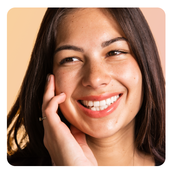 Una mujer con piel bronceada, cabello castaño y labios rosados con una sonrisa brillante y blanca, mirando hacia un lado.
