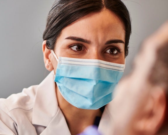 Female dentist wearing a face mask attentively consulting with a patient, emphasizing personalized dental care and expertise.