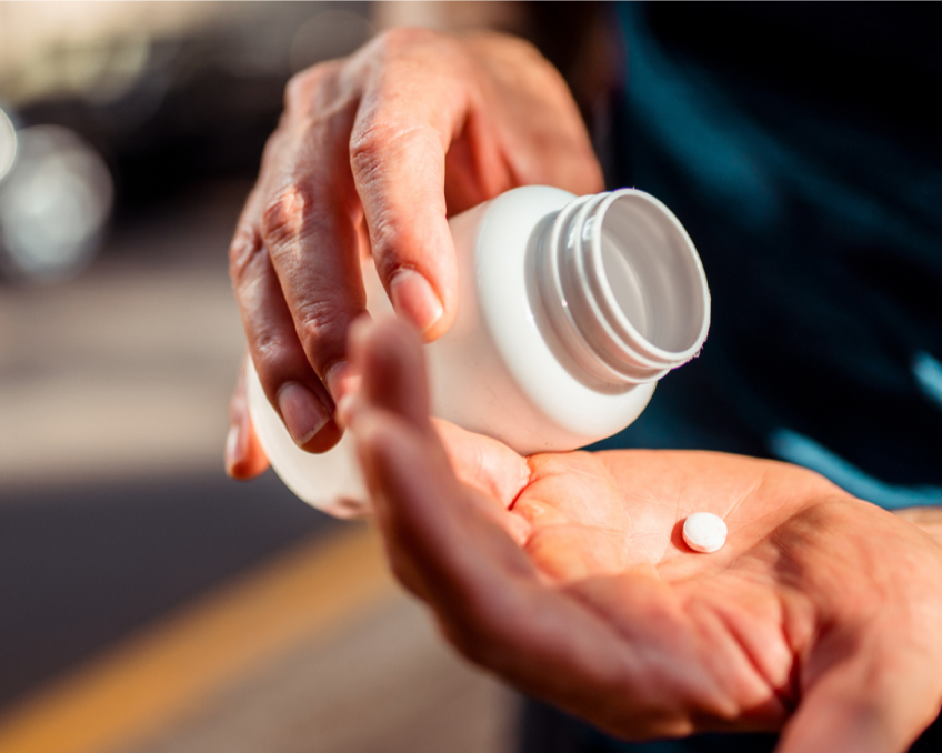 A person dispensing a pill from a white bottle into their hand.