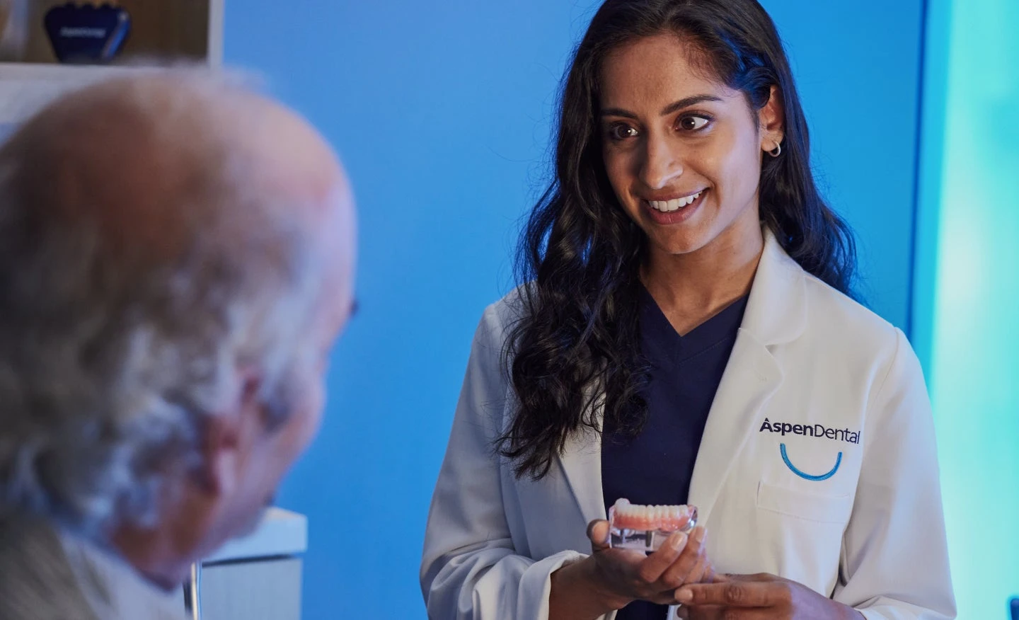 Aspen Dental professional holding a dentures model while consulting with an older patient about dental care options.