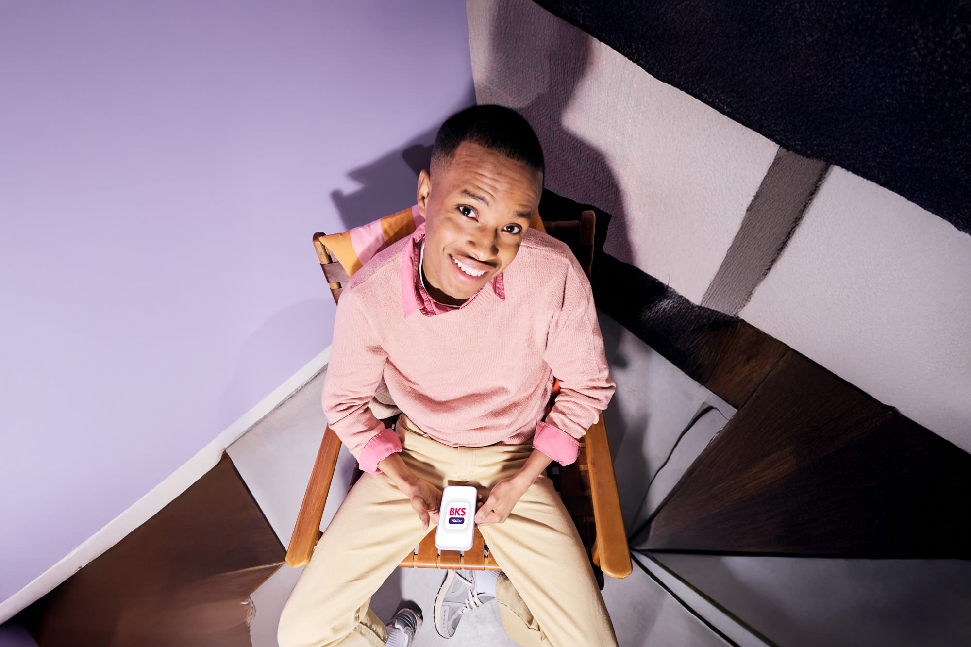 Junger Mann sitzt mit Smartphone in den Händen auf Stuhl – Smart bezahlen mit der BKS Bank Junger Mann sitzt mit Smartphone in den Händen auf Stuhl – Smart bezahlen mit der BKS Bank