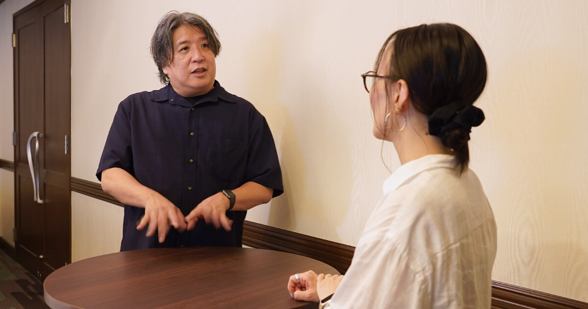会話風景（小山が話し、新山が聞く様子）
