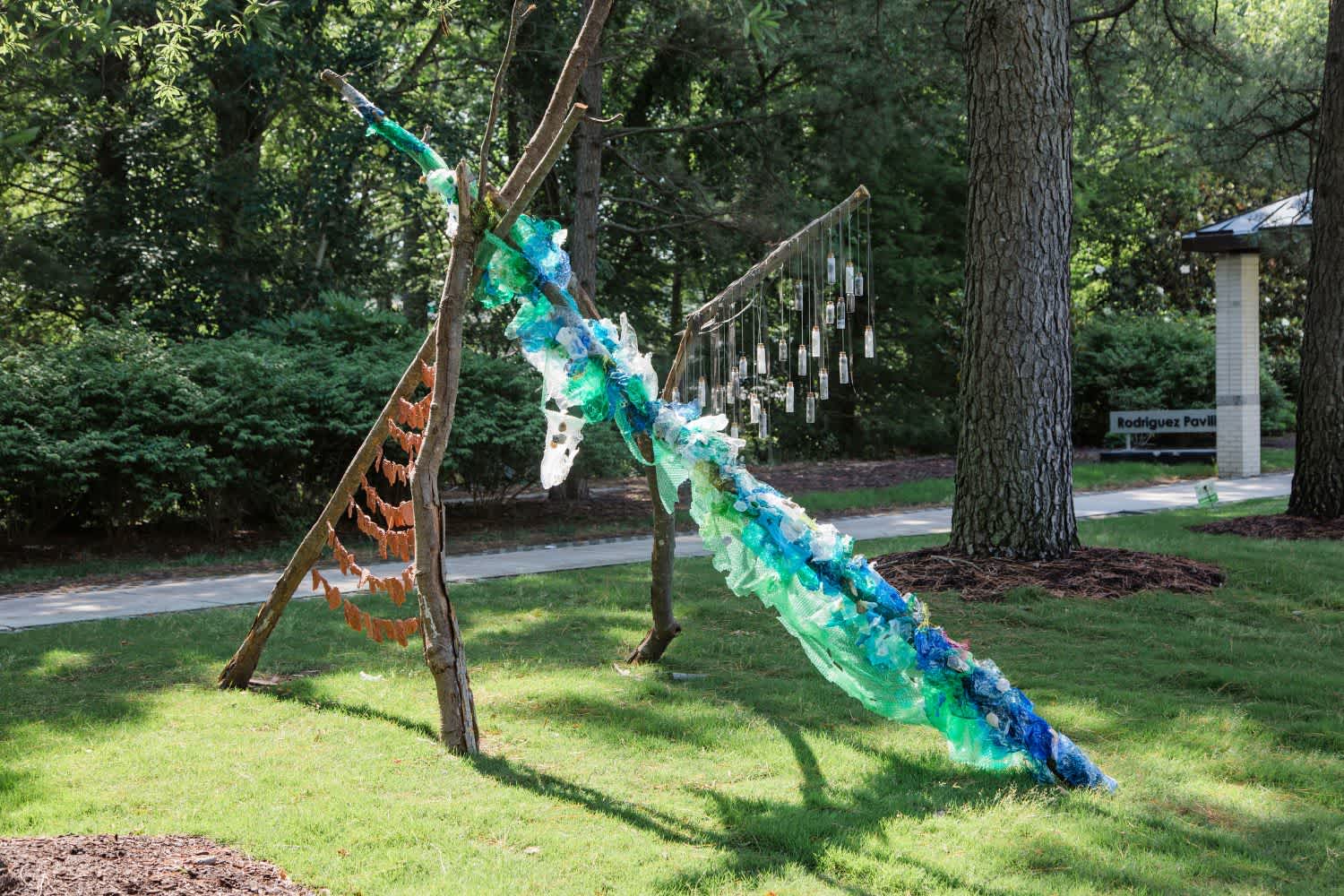 A structure made of three sticks, plastic, clay, and hanging bottles. 