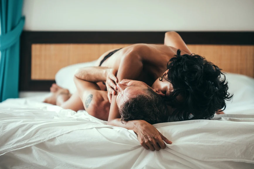 Couple having an intimate moment in bed, kissing, partially clothed.