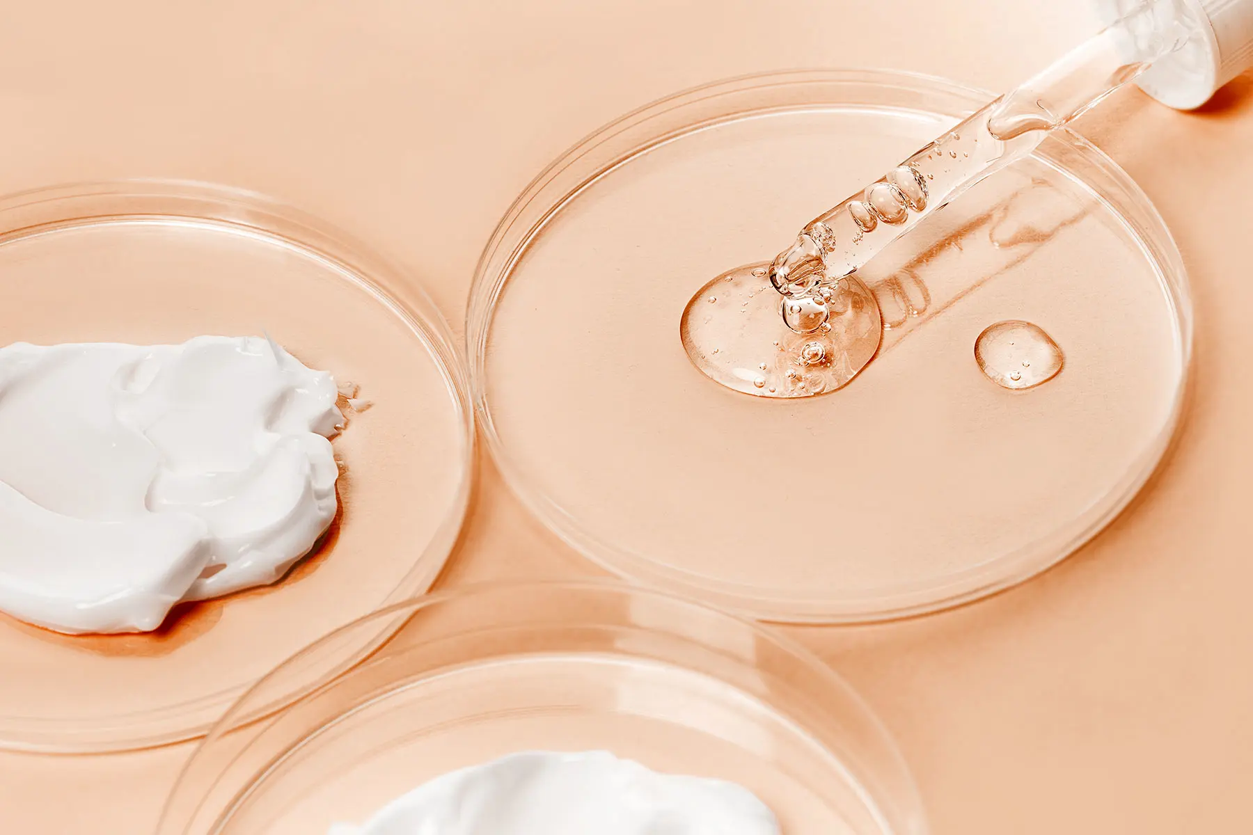 AW751 Pipette and Petri dishes with skin product formulations on peach colored background (header)