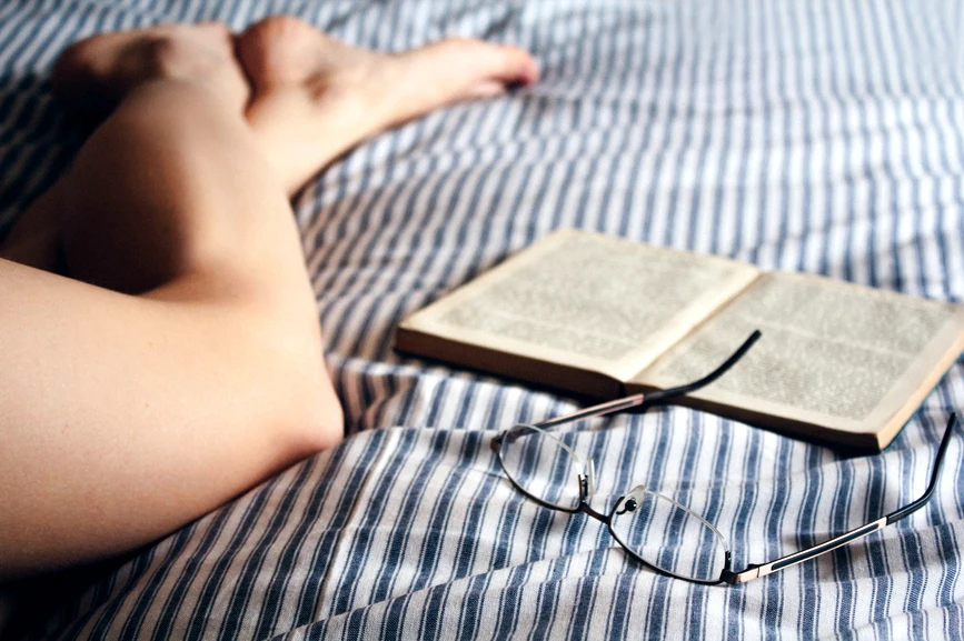 Womans legs in striped bedding with open book and eyeglasses beside her. AW286 