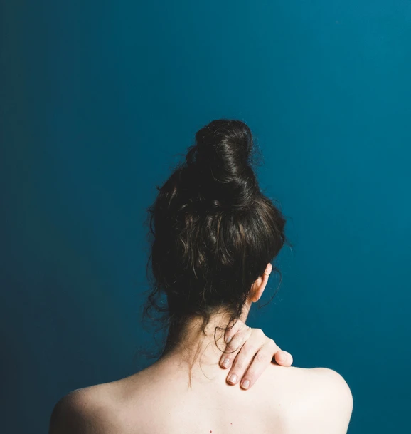 Rear view of woman - bare back - hand on neck facing blue wall. AW076