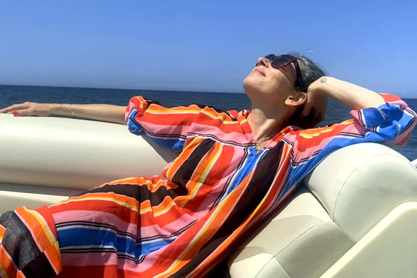 Stacy London in colorful striped caftan and sunglasses on boat, enjoying the breeze. AW516 