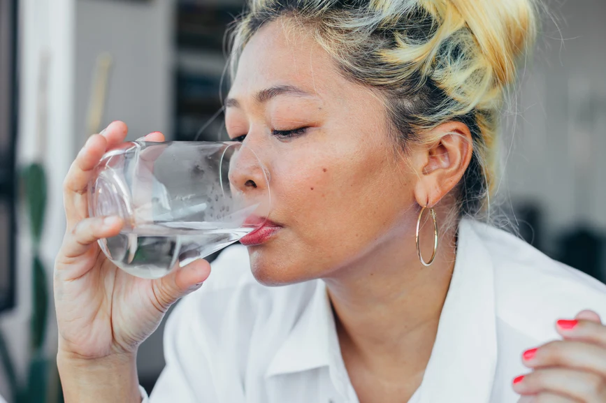 Asian woman with blonde hair drinking glass of water while on fast. AW201 