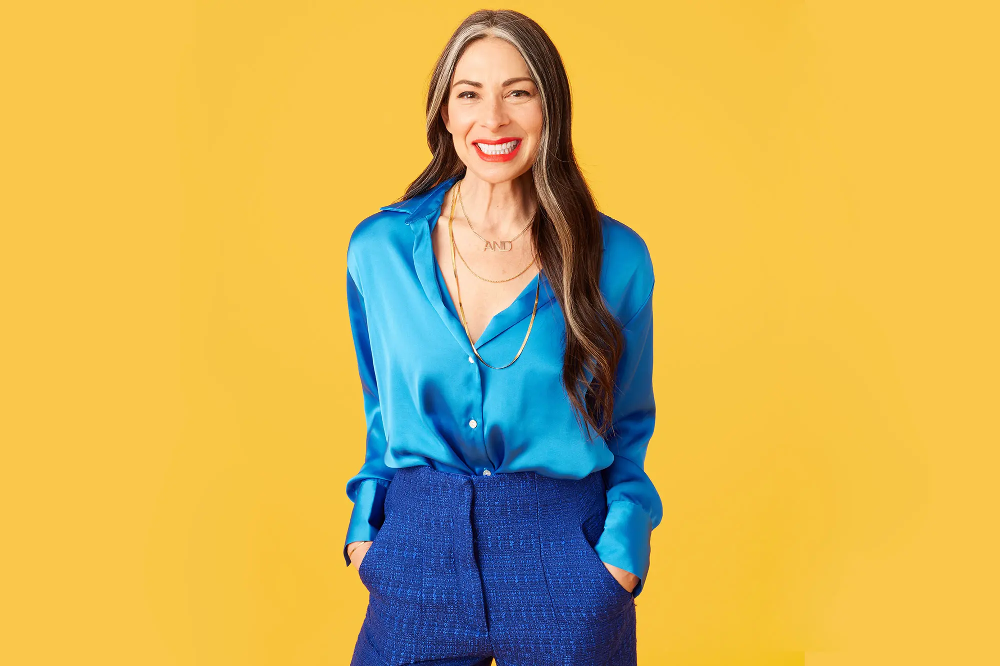 Stacy London dressed in vibrant blue, smiling on tangerine background. AW514