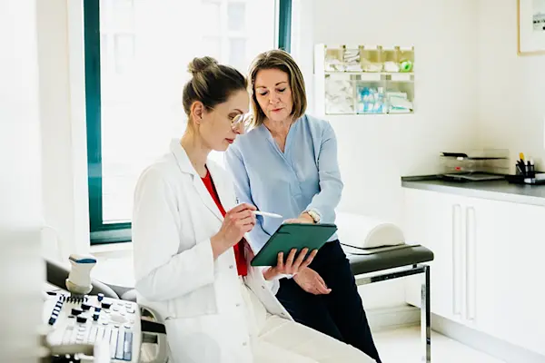 Middle aged female patient discussing medical history with female doctor in exam room. thumbnail