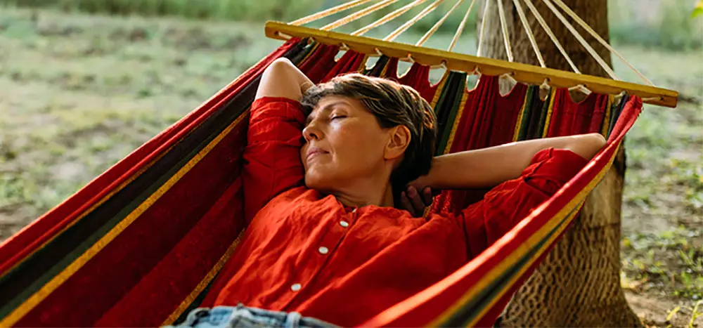 Woman dozing on a colorful hammock in the afternoon, eyes closed. AW247