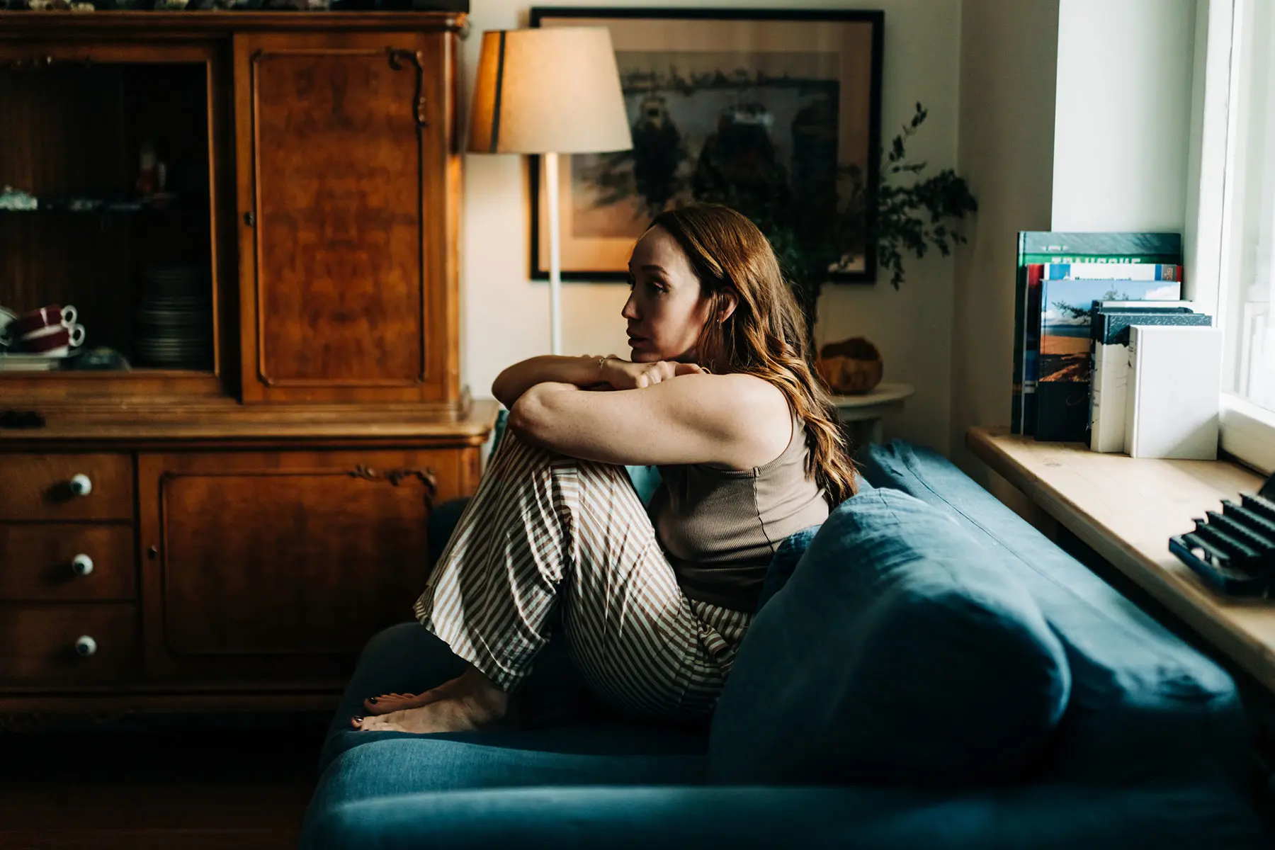 Woman sitting on a blue sofa, staring off in elegant room with her back to a window (top image)