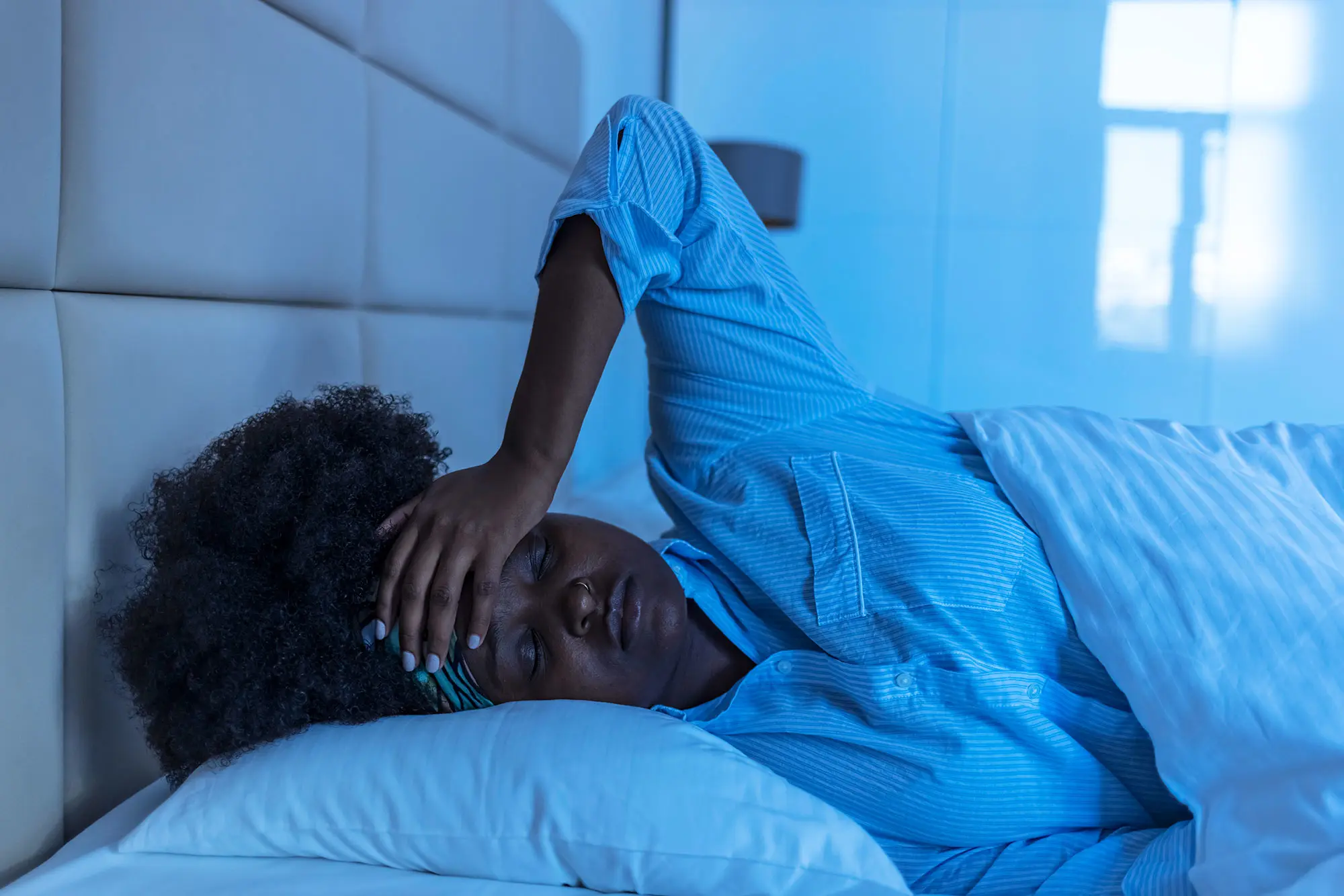 Black woman sleeping poorly, hand to her forehead in distress in the middle of the night. AW471