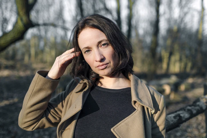 Woman in winter forest, hand brushing chin length brunette hair aside. AW250