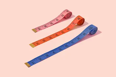 Tape measures in various colors showing different lengths on pale orange background. AW145