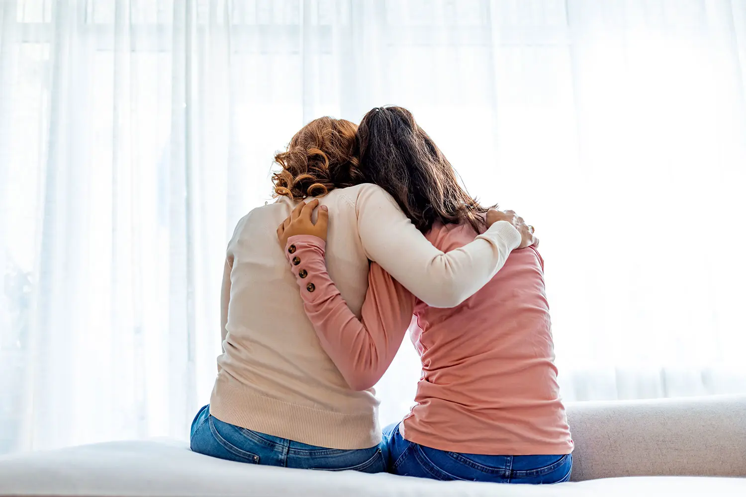 Teen daughter and mature mom from behind, sitting on bed embracing in support. AW518