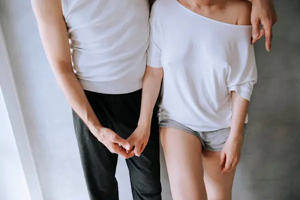 Couple cropped to midsection standing in a casual embrace holding hands in bedclothes. AW116